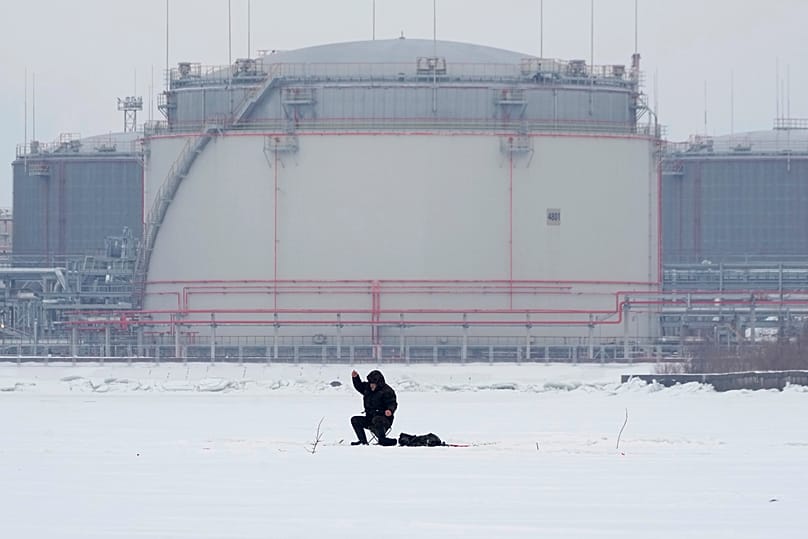 A man on the ice of the Gulf of Finland in St. Petersburg with oil storage tanks in the background, 12 February, 2024