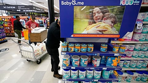 A grocery store worker stocks shelves behind a digital advertisement for a baby formula brand in Tijuana, Mexico.