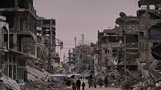 فلسطينيون يسيرون في شارع تحيط به مبانٍ مدمّرة جرّاء العمليات الجوية والبرية الإسرائيلية في خان يونس، جنوب قطاع غزة، الخميس 22 جانفي/يناير 2026. 