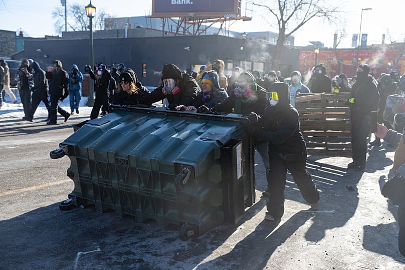 Protesters use a dumpster for cover as federal agents fire crowd control munitions at them after agents fatally shot Alex Pretti in Minneapolis on Saturday, 24 Jan 2026.
