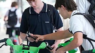 School boys use their phones as they rent bicycles in Sydney, Monday, 8 December, 2025.