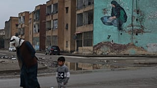 رجل وطفل يمشيان أمام لوحة جدارية في مبنى في الرقة, سوريا, السبت, يناير. 24, 2026. 