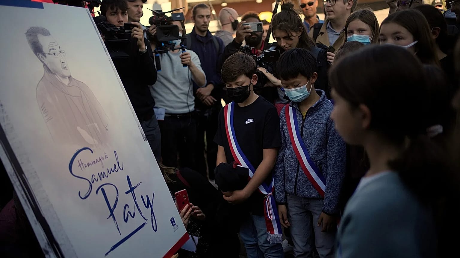 Children stand in front of a drawing of French history and geography teacher Samuel Paty in Conflans Sainte Honorine, 16 October, 2021