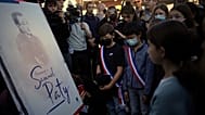 Children stand in front of a drawing of French history and geography teacher Samuel Paty in Conflans Sainte Honorine, 16 October, 2021