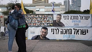 Two women embrace next to a banner with a photo of Ran Gvili in Tel Aviv, 26 January, 2026