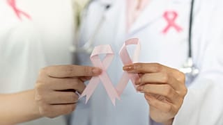 يدان تمسكان بشريطين ورديين، الرمز العالمي للتوعية بسرطان الثدي.