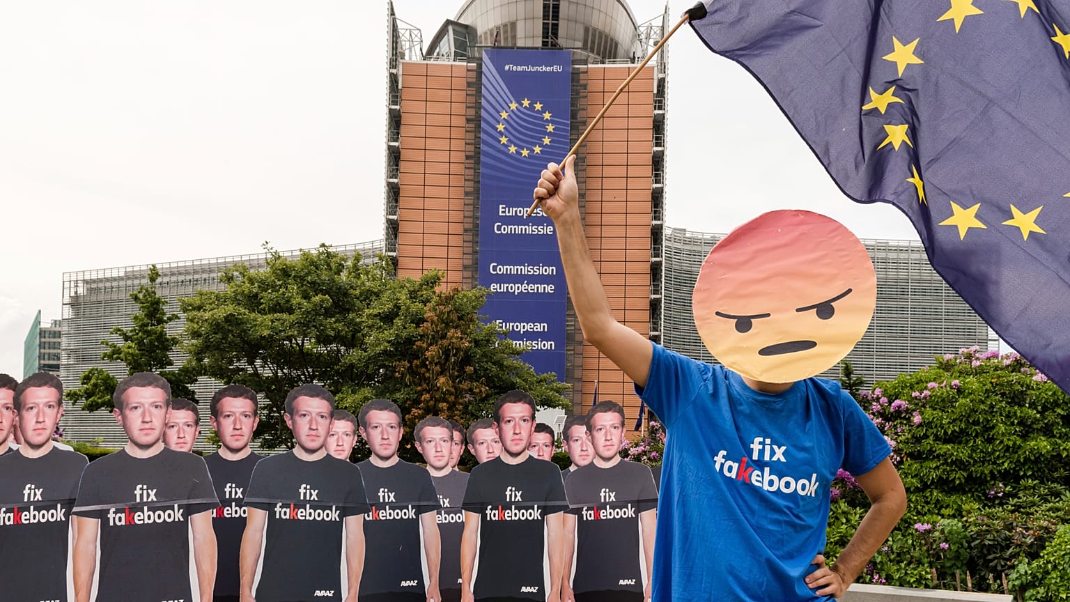 Un activista de Avaaz agita la bandera europea junto a cartones a tamaño real de Zuckerberg para protestar contra las cuentas falsas de Facebook que difunden desinformación