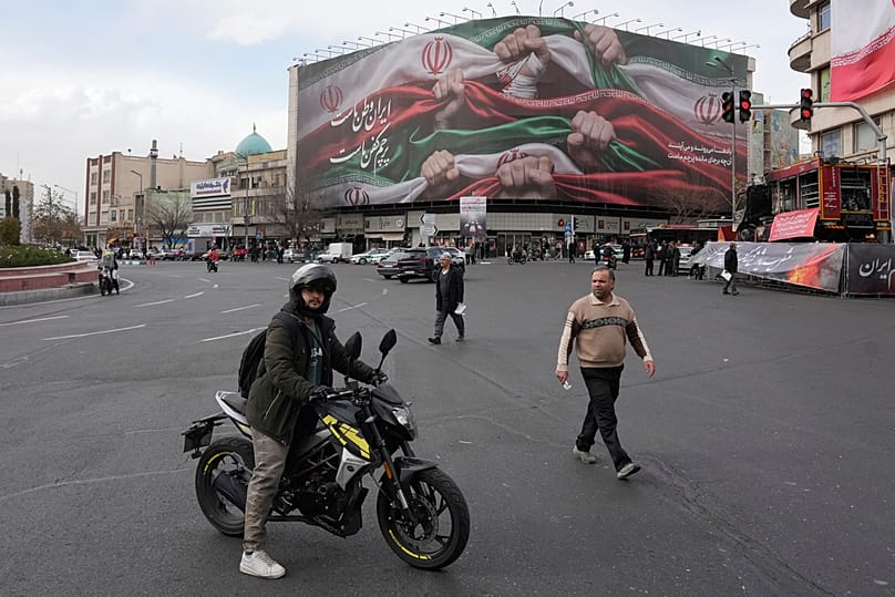 FILE: A man stands with his motorbike in front of a huge banner showing hands holding Iranian flags as a sign of patriotism, in Tehran, 14 January 2026