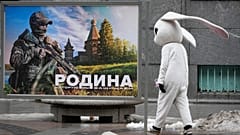 DATEI: Ein Straßenkünstler geht an einem patriotischen Plakat vorbei, das einen russischen Soldaten und den Slogan "Das Mutterland, das wir verteidigen" zeigt, in St. Petersburg, Russland, 14. März 2023
