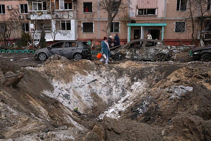 People pass a crater and damaged cars near an apartment building after a Russian attack in Zaporizhzhia, 28 January, 2026