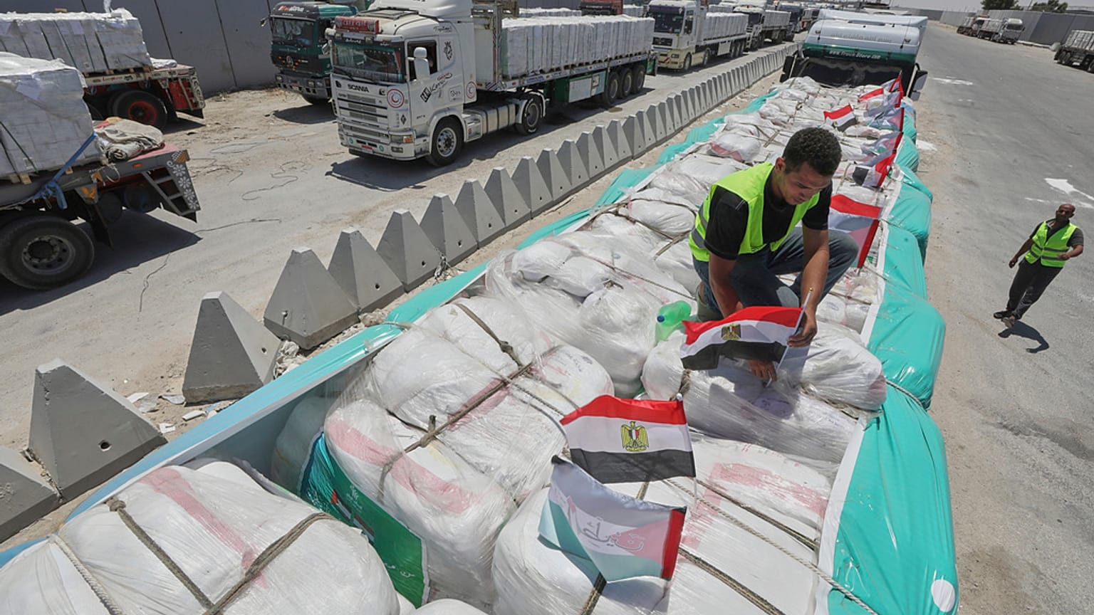 عامل يعلّق أعلام مصر على شحنة مساعدات إنسانية على شاحنة استعدادًا لدخولها عبر معبر رفح بين مصر وقطاع غزة، الأربعاء 6 أغسطس 2025.