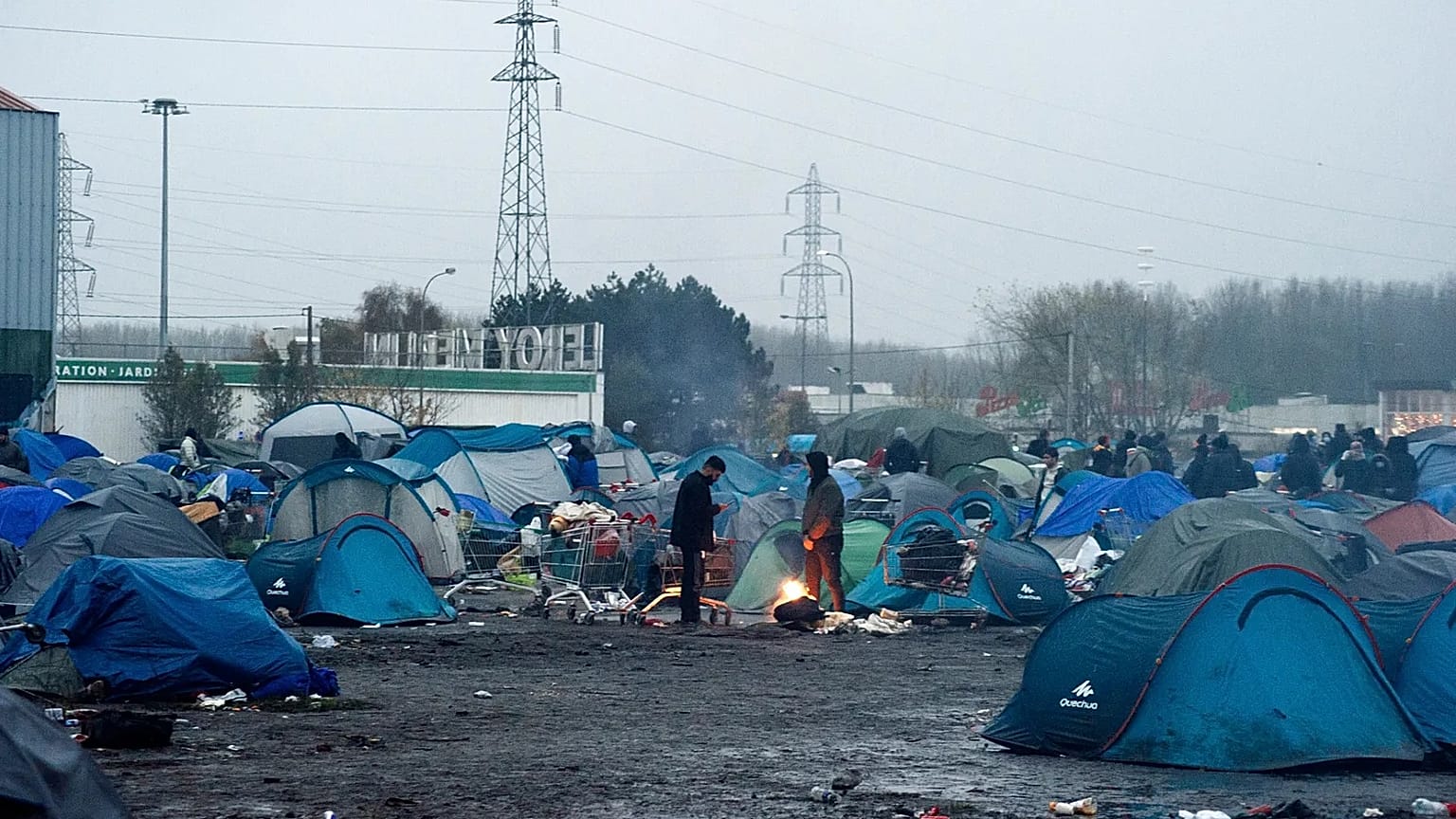 Migrants warm by a fire in a camp in Grande-Synthe, Northern France, Tuesday, Nov. 16, 2021