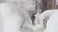 Un homme marche sous un parapluie au milieu de grandes congères lors de fortes chutes de neige, à Minamiuonuma, préfecture de Niigata, Japon, le 29 janvier 2026