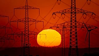 Die Sonne geht am 15. Mai 2022 am Stadtrand von Frankfurt am Main hinter Strommasten auf.