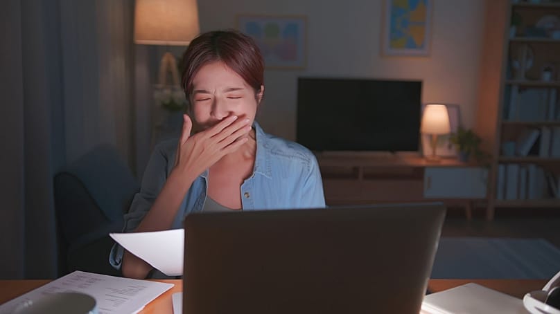 Une jeune fille travaillant sur son ordinateur portable la nuit et montrant des signes de fatigue.
