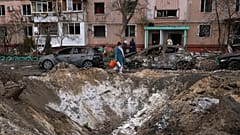 Ukrayna’nın Zaporijya kentinde, Rusya’nın düzenlediği saldırının ardından bir apartman binası yakınında hasar gören araçların yanından geçen insanlar, 28 Ocak 2026.