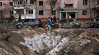 Ukrayna’nın Zaporijya kentinde, Rusya’nın düzenlediği saldırının ardından bir apartman binası yakınında hasar gören araçların yanından geçen insanlar, 28 Ocak 2026.