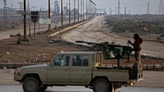 مقاتل من قوات سورية الديمقراطية (SDF) يقف على شاحنة بيك أب، مع طريق يؤدي نحو خط المواجهة في الخلفية، وذلك قبيل انتهاء هدنة مدتها أربعة أيام مع الحكومة السورية في محافظة الحسكة