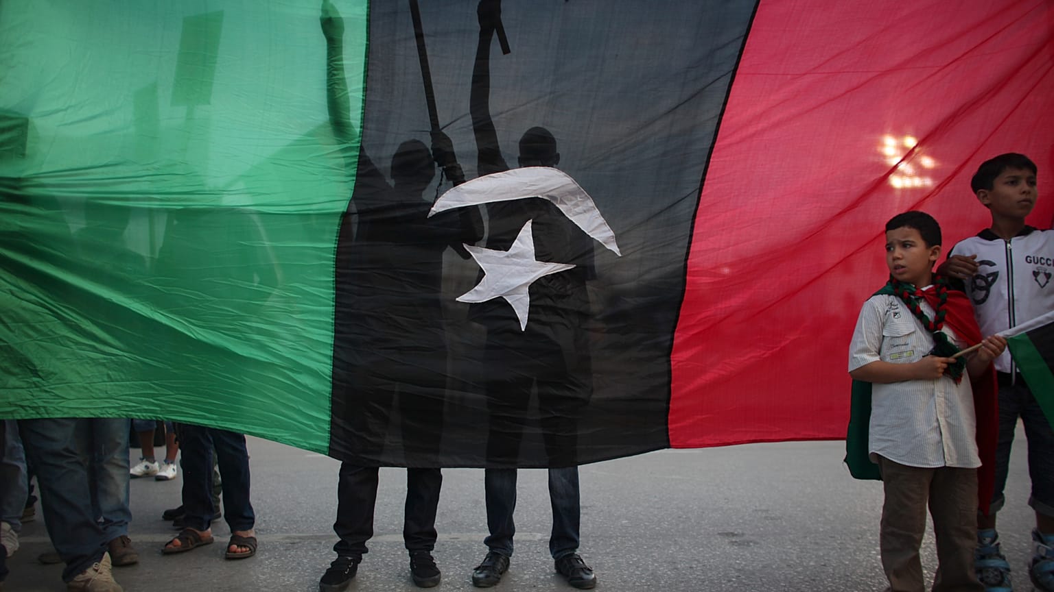 يقف صبية أمام المتظاهرين، من خلف علم يعود إلى ما قبل عهد القذافي، احتجاجاً على وجود الأسلحة في طرابلس، ليبيا، يوم الجمعة 30 سبتمبر 2011. (صورة من وكالة أسوشيتد برس/ألكسندر مين