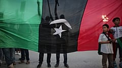 يقف صبية أمام المتظاهرين، من خلف علم يعود إلى ما قبل عهد القذافي، احتجاجاً على وجود الأسلحة في طرابلس، ليبيا، يوم الجمعة 30 سبتمبر 2011. (صورة من وكالة أسوشيتد برس/ألكسندر مين