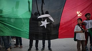 يقف صبية أمام المتظاهرين، من خلف علم يعود إلى ما قبل عهد القذافي، احتجاجاً على وجود الأسلحة في طرابلس، ليبيا، يوم الجمعة 30 سبتمبر 2011. (صورة من وكالة أسوشيتد برس/ألكسندر مين