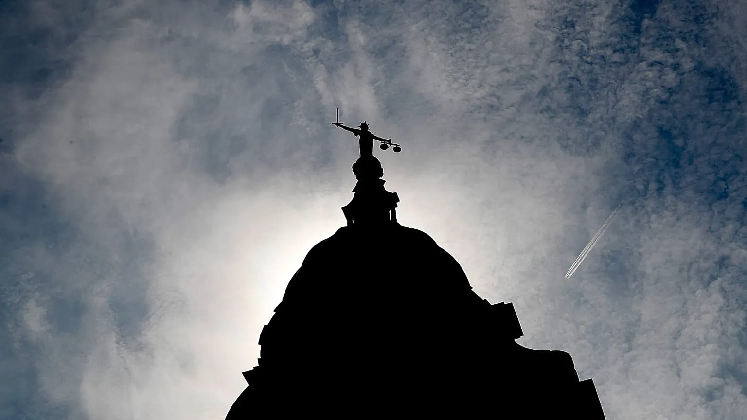 A statue of liberty is silhouetted as it stands atop the Old Bailey in London, 8 August, 2019