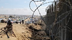 Palestinos desplazados por la ofensiva aérea y terrestre de Israel en la Franja de Gaza se sientan junto a la valla fronteriza con Egipto en Rafah, el 24 de enero de 2024.