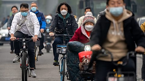 FOTO DE ARCHIVO - Vagabundos con mascarillas circulan en bicicleta por una calle del distrito financiero central de Pekín, el jueves 20 de octubre de 2022. (AP Photo/Mark Schiefelbein, archivo