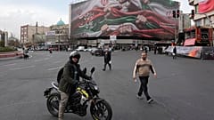 رجل يقف مع دراجته النارية أمام لافتة ضخمة تُظهر أيديًا تمسك بالأعلام الإيرانية تعبيرًا عن الوطنية، في طهران، إيران، يوم الأربعاء 14 يناير 2026. (صورة أسوشيتد برس/ وحيد سالمی)