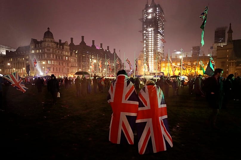 Persone avvolte in bandiere del Regno Unito attraversano Parliament Square durante la pioggia a Londra, 31 gennaio 2020