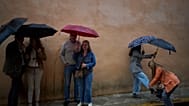 Unas cuantas personas se refugian de la lluvia bajo sus paraguas en una foto de la Semana Santa de Andalucía de 2025