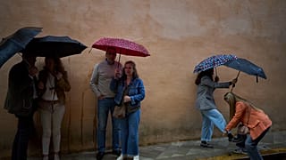 Unas cuantas personas se refugian de la lluvia bajo sus paraguas en una foto de la Semana Santa de Andalucía de 2025