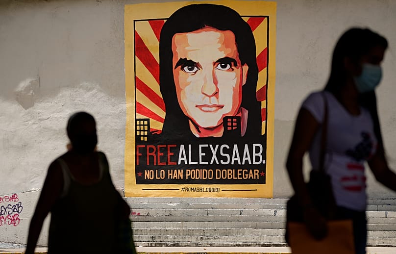 ARCHIVO - Peatones caminan cerca de un cartel que pide la libertad del empresario colombiano y enviado especial venezolano Alex Saab, en Caracas, el 9 de septiembre de 2021.