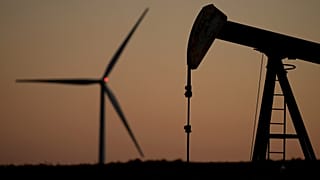 Una bomba de petróleo funciona en primer plano mientras un aerogenerador del parque eólico Buckeye se alza al fondo, el 30 de septiembre de 2024 cerca de Hays, Kansas.