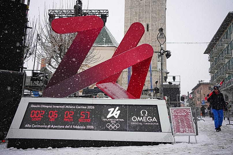 Ludzie przechodzą obok logo Zimowych Igrzysk Milano Cortina 2026 z ekranem odliczającym w Cortina d’Ampezzo, Włochy, środa, 4 lutego 2026 r.