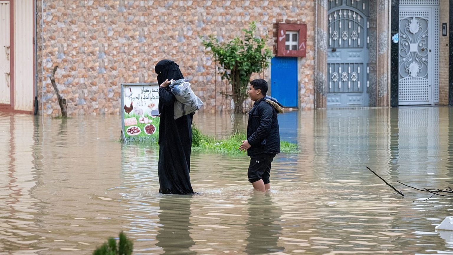 Şiddetli yağışın ardından Fas’ın Ksar El Kebir kentinde su basmış bir caddeden tahliye edilen bir anne ve oğlu, 30 Ocak 2026