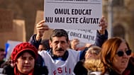 A man holds a paper that reads "The educated human is no longer in demand" as teachers and education system employees take part in a protest against planned austerity measures