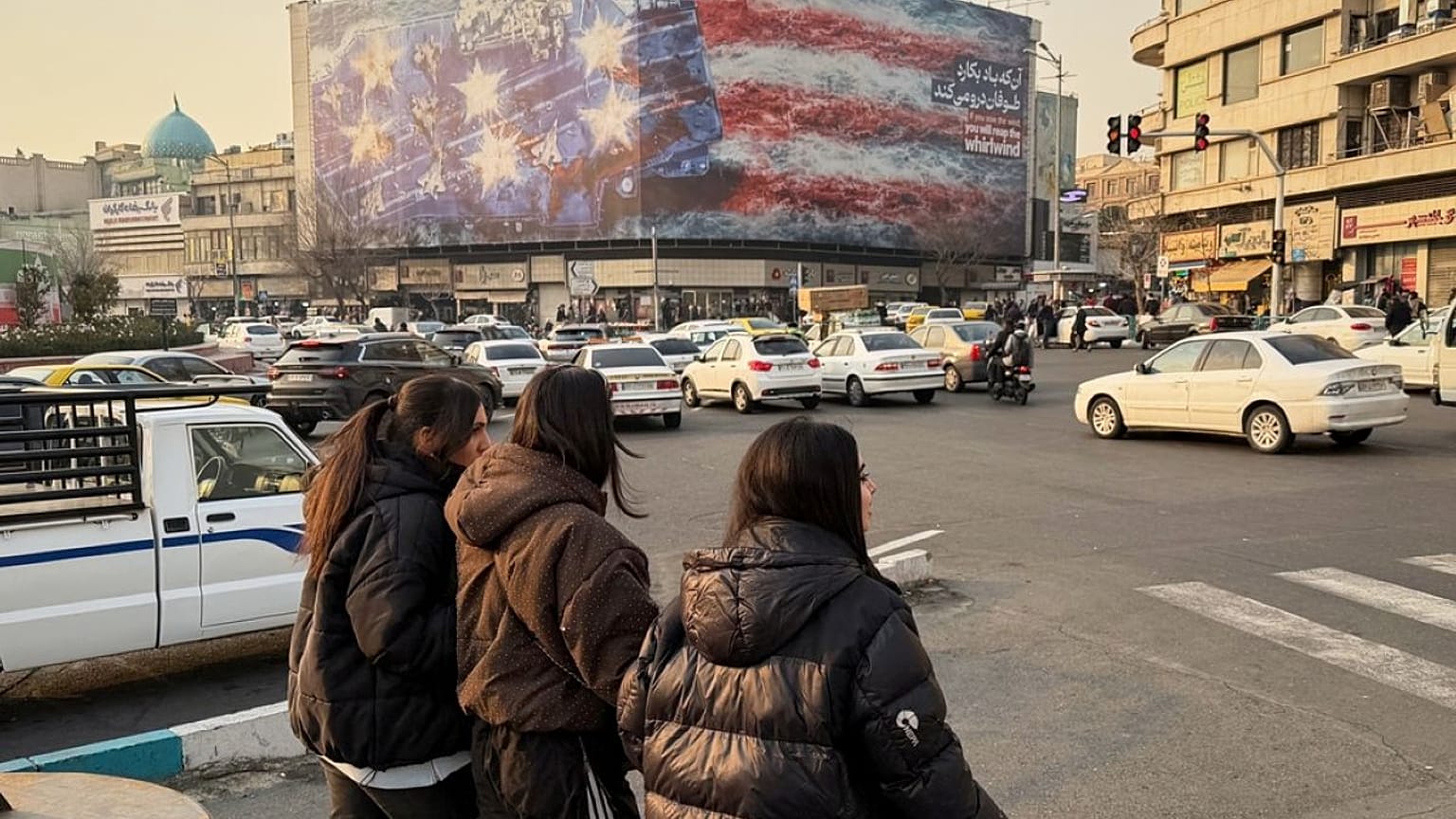 يسير الناس أمام لوحة إعلانية تحمل صورة حاملة طائرات أمريكية عليها طائرات مقاتلة متضررة، في ميدان انقلاب إسلامي في طهران، إيران، الأحد 25 يناير/كانون الثاني 2026. 