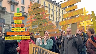 People protesting against the environmental and economic unsustainability of the 2026 Milan-Cortina Winter Olympics holding up signs in Milan on 7 February 2026.