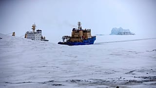 FILE - An Icebreaker makes the path for a cargo ship with an iceberg in the background near a port on the Alexandra Land island near Nagurskoye, Russia, May 17, 2021. 