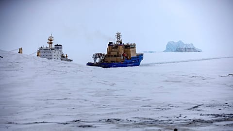 FILE - An Icebreaker makes the path for a cargo ship with an iceberg in the background near a port on the Alexandra Land island near Nagurskoye, Russia, May 17, 2021. 