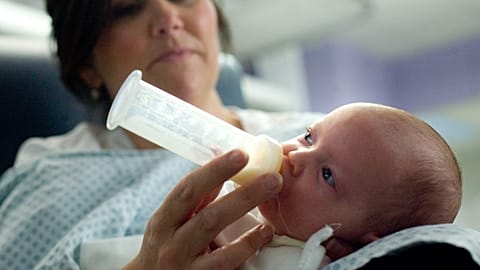 Um bebé que recebe um biberão feito de leite em pó 