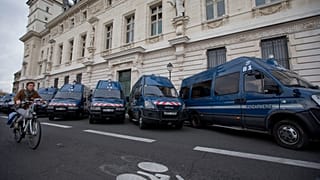 Une cycliste passe devant des véhicules de la police française devant le tribunal correctionnel du Quai des Orfèvres à Paris, le lundi 16 novembre 2015