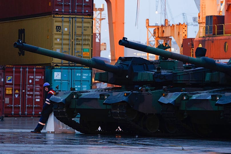 A worker stands next to South Korean Black Panther K2 tanks in in the Polish Navy port of Gdynia, Poland, Tuesday, Dec. 6, 2022.