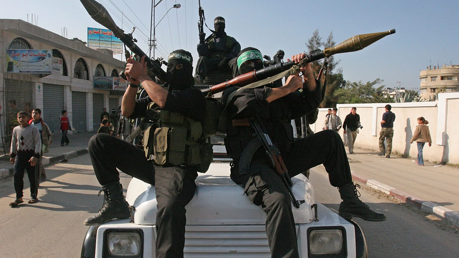 مسلحون فلسطينيون من حركة حماس، يرتدون الأقنعة ويحملون قاذفات قنابل، يستقلون شاحنة في شوارع مدينة غزة.