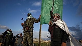 صبي يحمل سلاحًا بجانب مقاتل من حماس قبل تسليم أربعة جثث للصليب الأحمر في خانيونس جنوب غزة، الخميس 20 فبراير 2025.