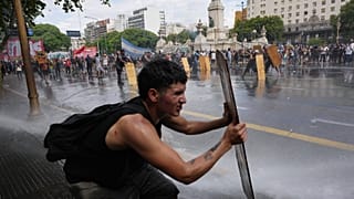 Manifestantes se protegen con tablones de madera mientras la Policía lanza agua durante choques en una marcha sindical contra la reforma laboral del Gobierno de Milei.