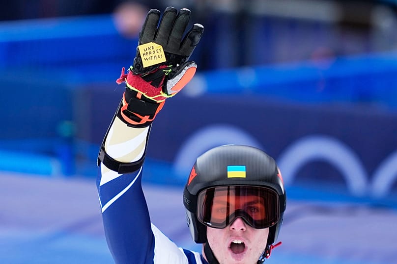 Ukraine's Dmytro Shepiuk holds a sticker reading "UKR heroes with us", at the finish area, during a men's super-G race, at 2026 Winter Olympics, Bormio, Italy, Feb.11, 2026