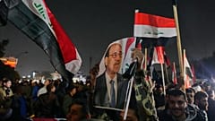 رجل عراقي يحمل صورة رئيس الوزراء السابق نوري المالكي، خلال احتجاج ضد الرئيس دونالد ترامب على جسر يؤدي إلى المنطقة الخضراء المحصنة حيث تقع السفارة الأمريكية في بغداد، 
