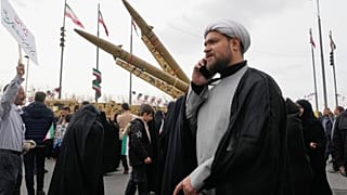 صورة تعبيرية- رجل دين يتحدث على هاتفه أثناء سيره أمام صواريخ محلية الصنع خلال مسيرة سنوية لإحياء ذكرى الثورة الإسلامية عام 1979 في ساحة آزادي